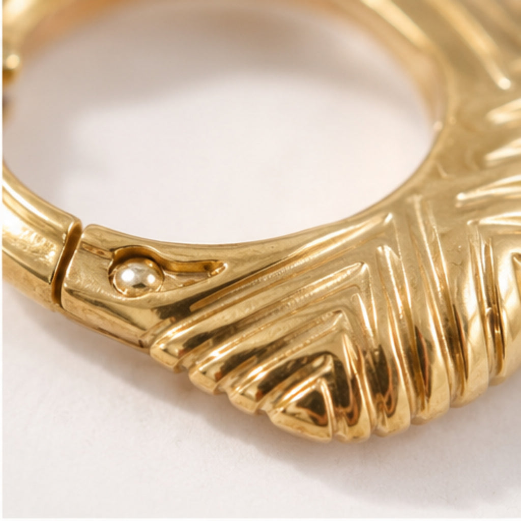 Close-up of a gold-toned ring with a textured, ribbed outer surface and a small raised gold bead detail near the clasp, shown on a plain light background.
