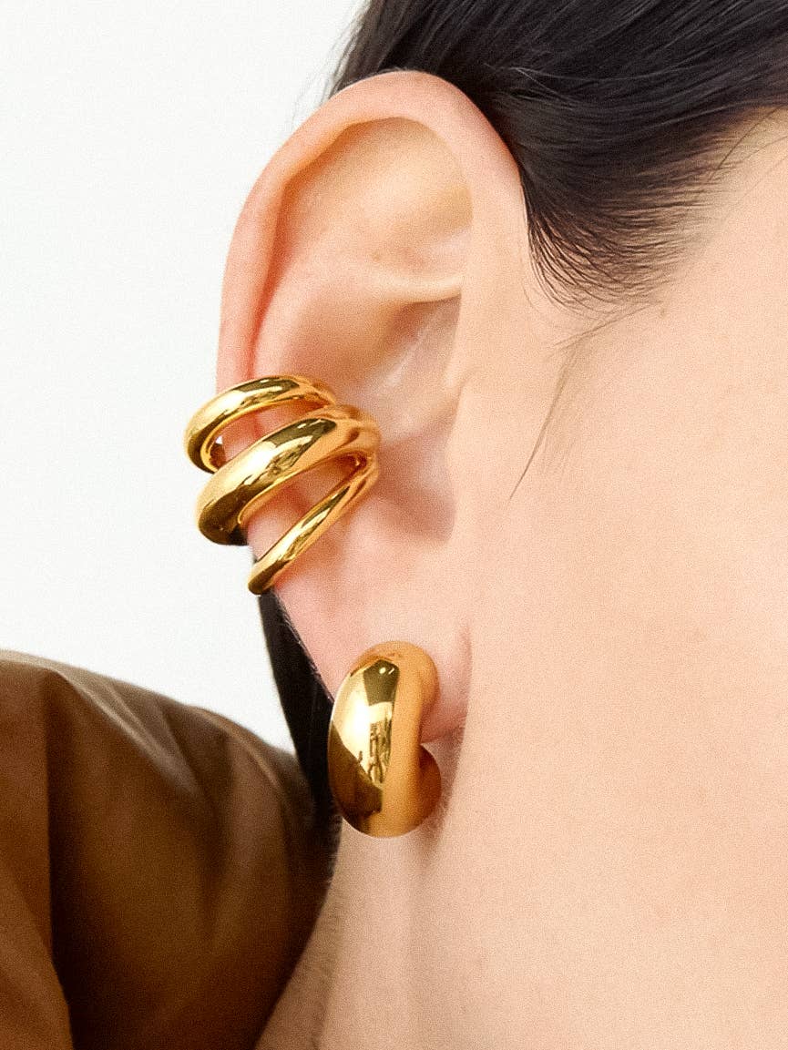 Gold spiral earring worn on an ear with a plain background