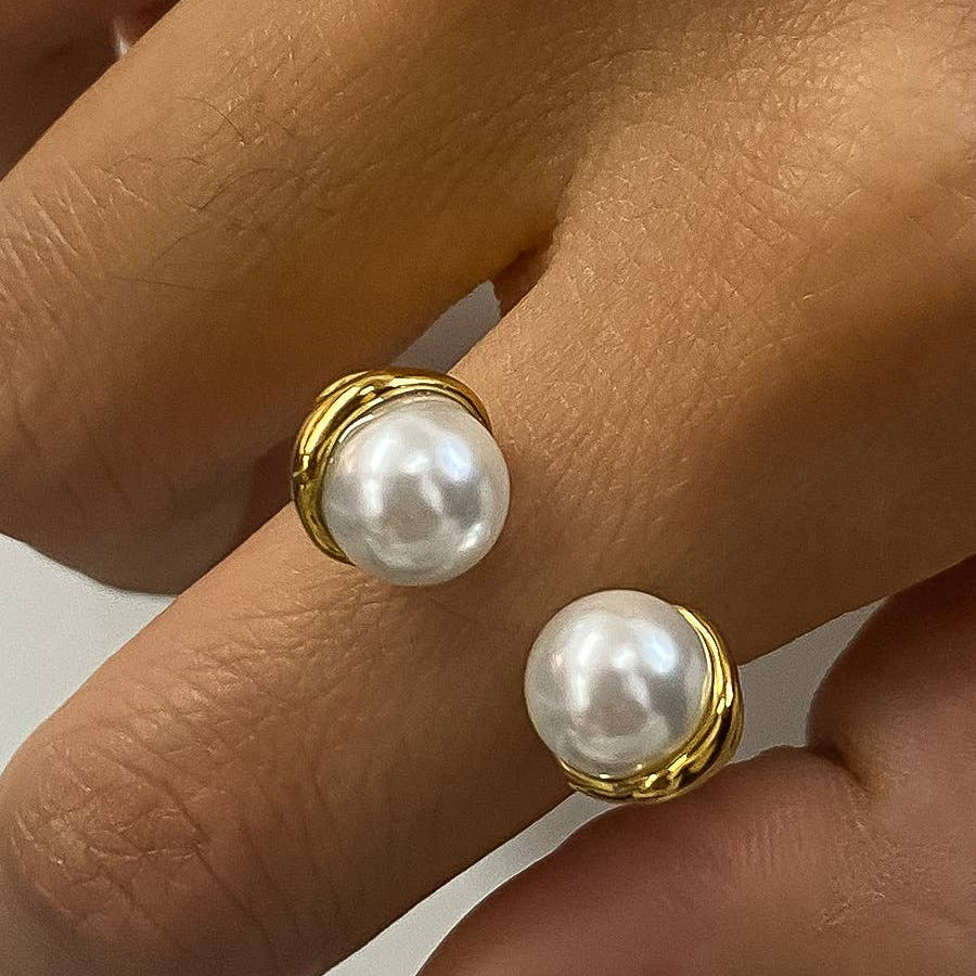 Pearl earrings with gold posts held between fingers against a neutral background