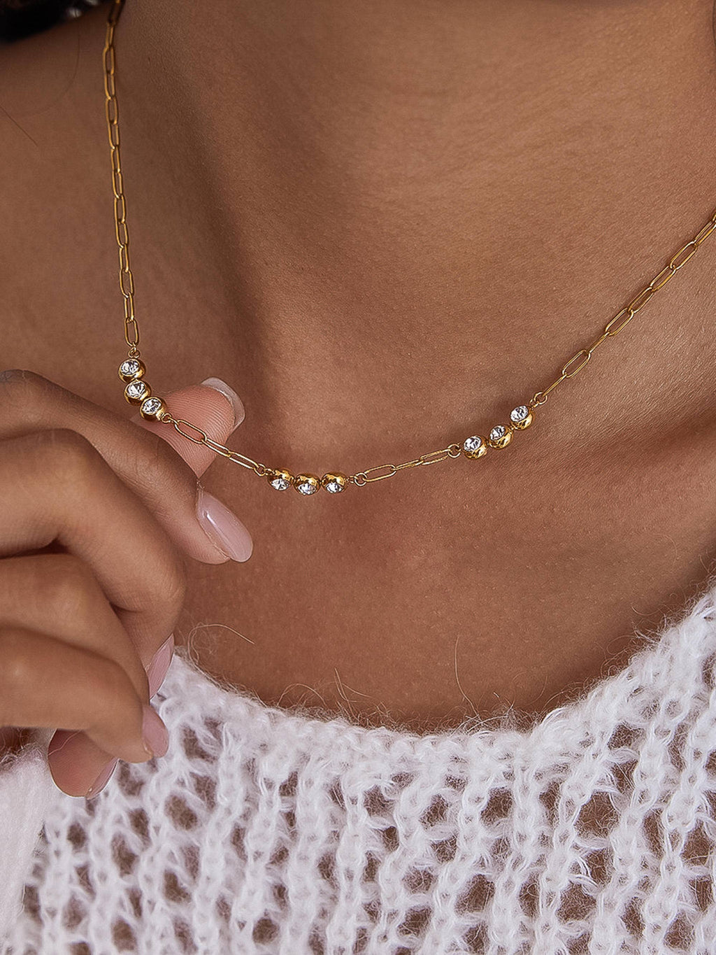 Gold necklace with small pearls worn by a person with a white lace garment.