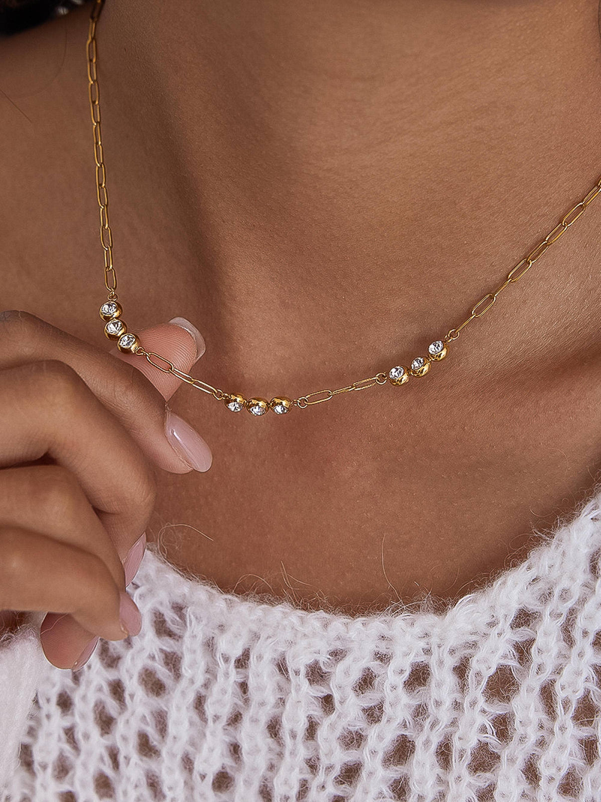 Gold necklace with small pearls worn by a person with a white lace garment.