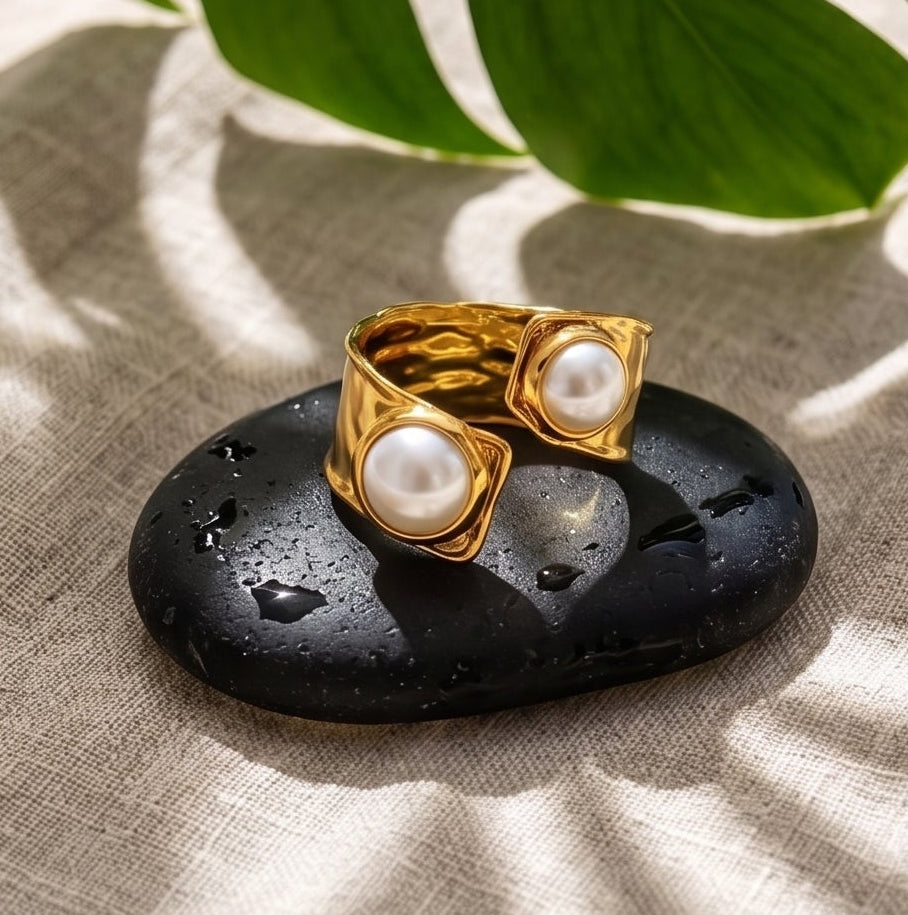 A four-panel collage showing a gold ring with large white pearl-like stones worn on a hand, plus the same ring displayed on a black stone and floating in shallow water. The scenes include a beach driftwood setting, a bowl of water with flowers, and a beach background, indicating a lifestyle presentation.