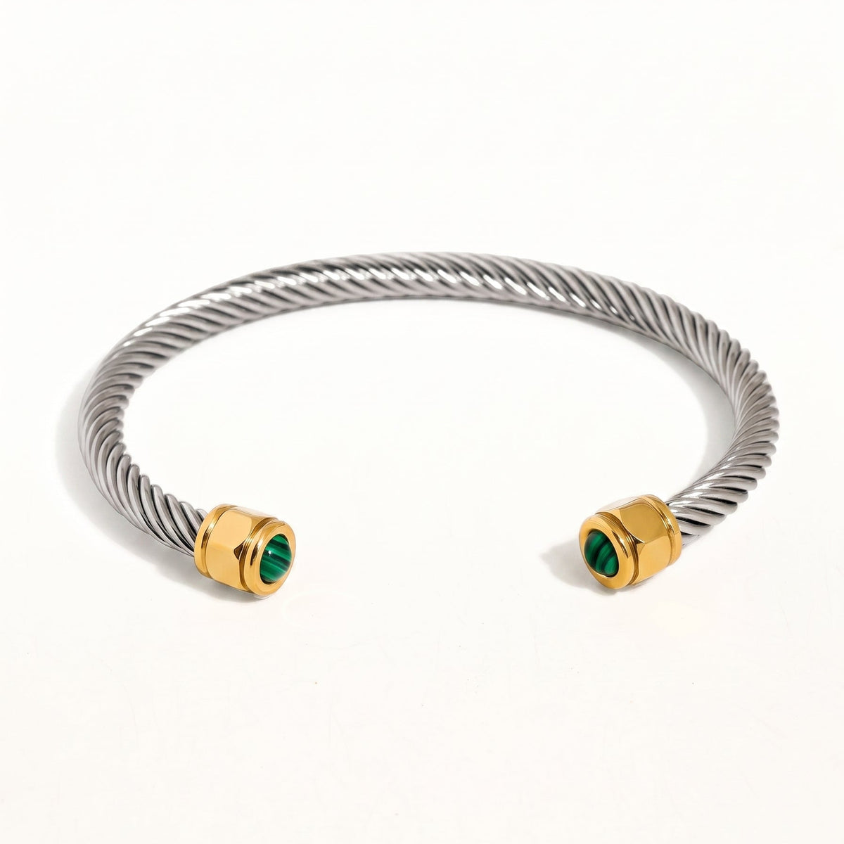 A silver-toned twisted cable cuff bracelet with gold-toned end caps and small green stone accents, photographed on a clean white background.