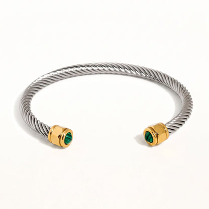 Meris Bracelet in Silver, a silver-tone twisted cable cuff with gold-tone end caps and small green stone accents, on a white background