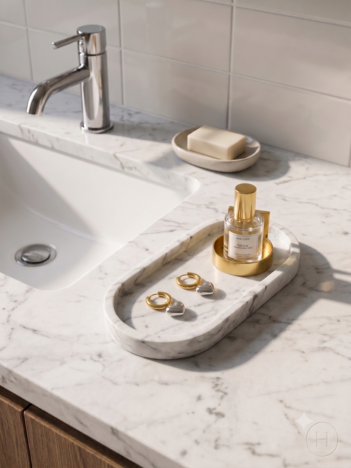 A marble bathroom vanity tray with a gold-toned ring holder, holding three rings, set on a white marble countertop next to a sink and soap dish.