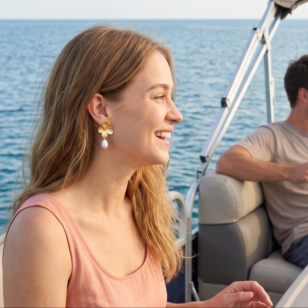 A woman in a peach dress sits on a boat seat beside a gray table with a map and gold compass, smiling as a man and another woman laugh in the background on the water.
