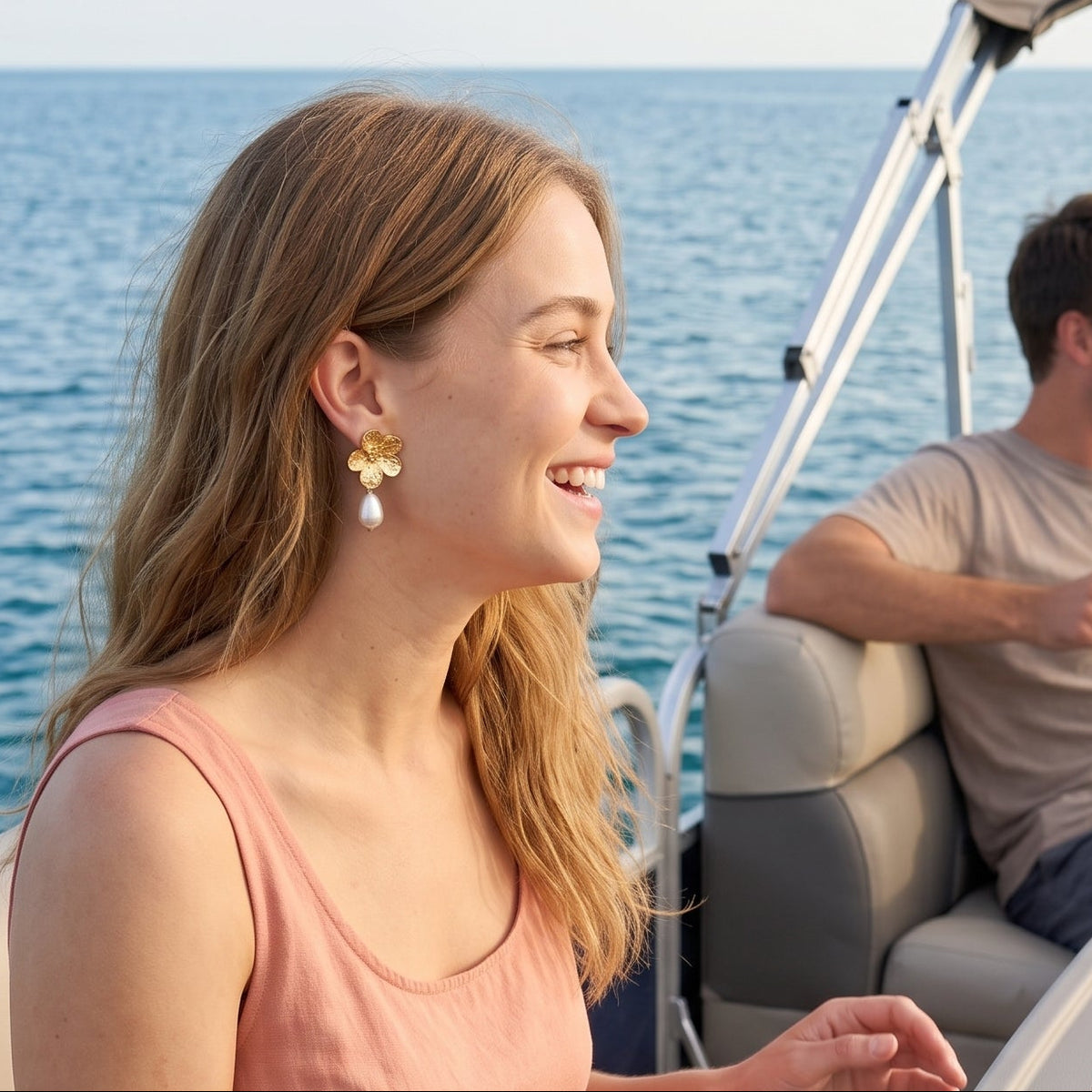 A woman in a peach dress sits on a boat seat beside a gray table with a map and gold compass, smiling as a man and another woman laugh in the background on the water.
