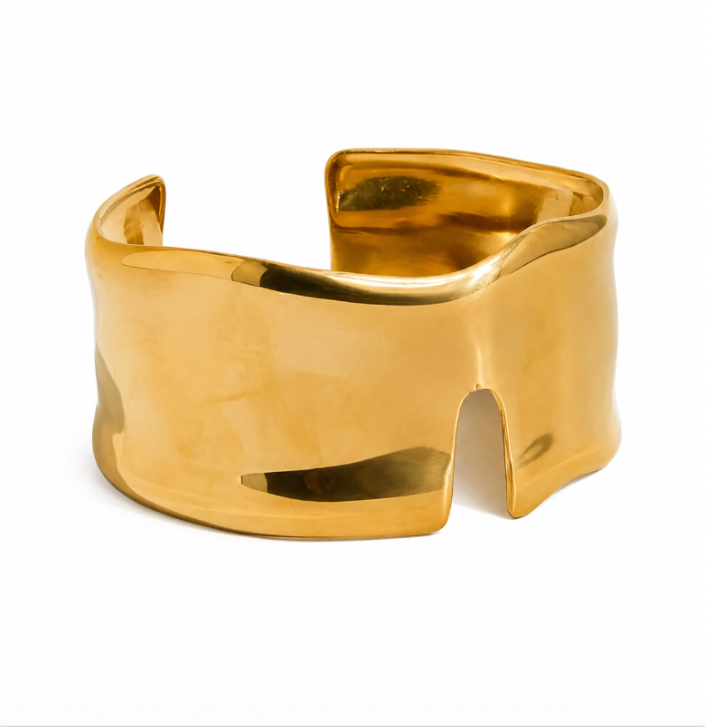 A wide, polished gold cuff bracelet with a sculptural, organic wavy shape, photographed on a clean white background.