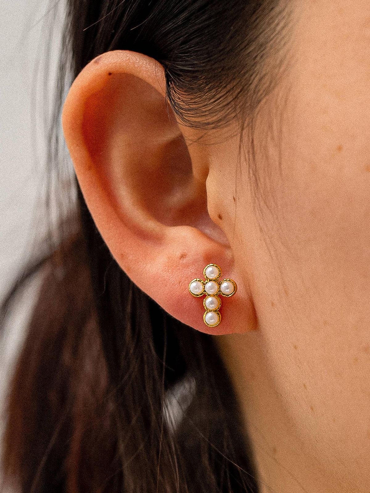 Close-up of an ear wearing a gold earring with pearl-like stones on a neutral background